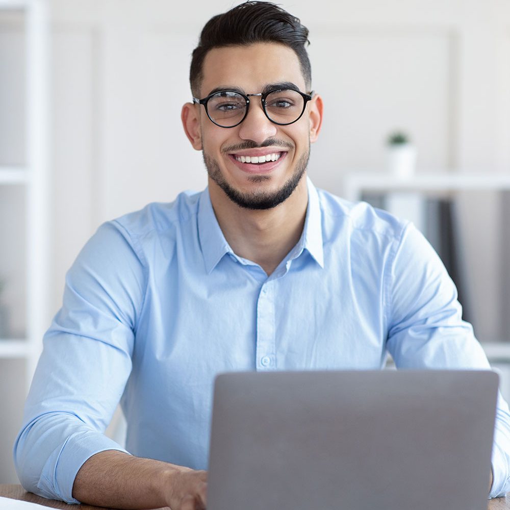 happy-young-arab-businessman-in-glasses-sitting-at-9RGN9Y5.jpg